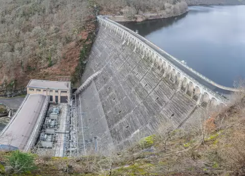 Le mur courbe du barrage de Sarrans et son usine au pied, avec le lac de retenue en amont