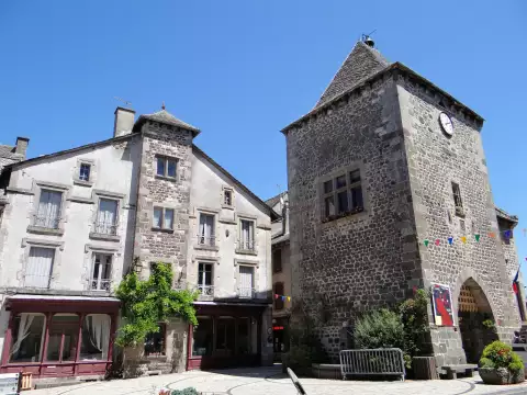 La tour de Monaco, porte de ville en basalte de Mur-de-Barrez, à côté d'une maison ancienne