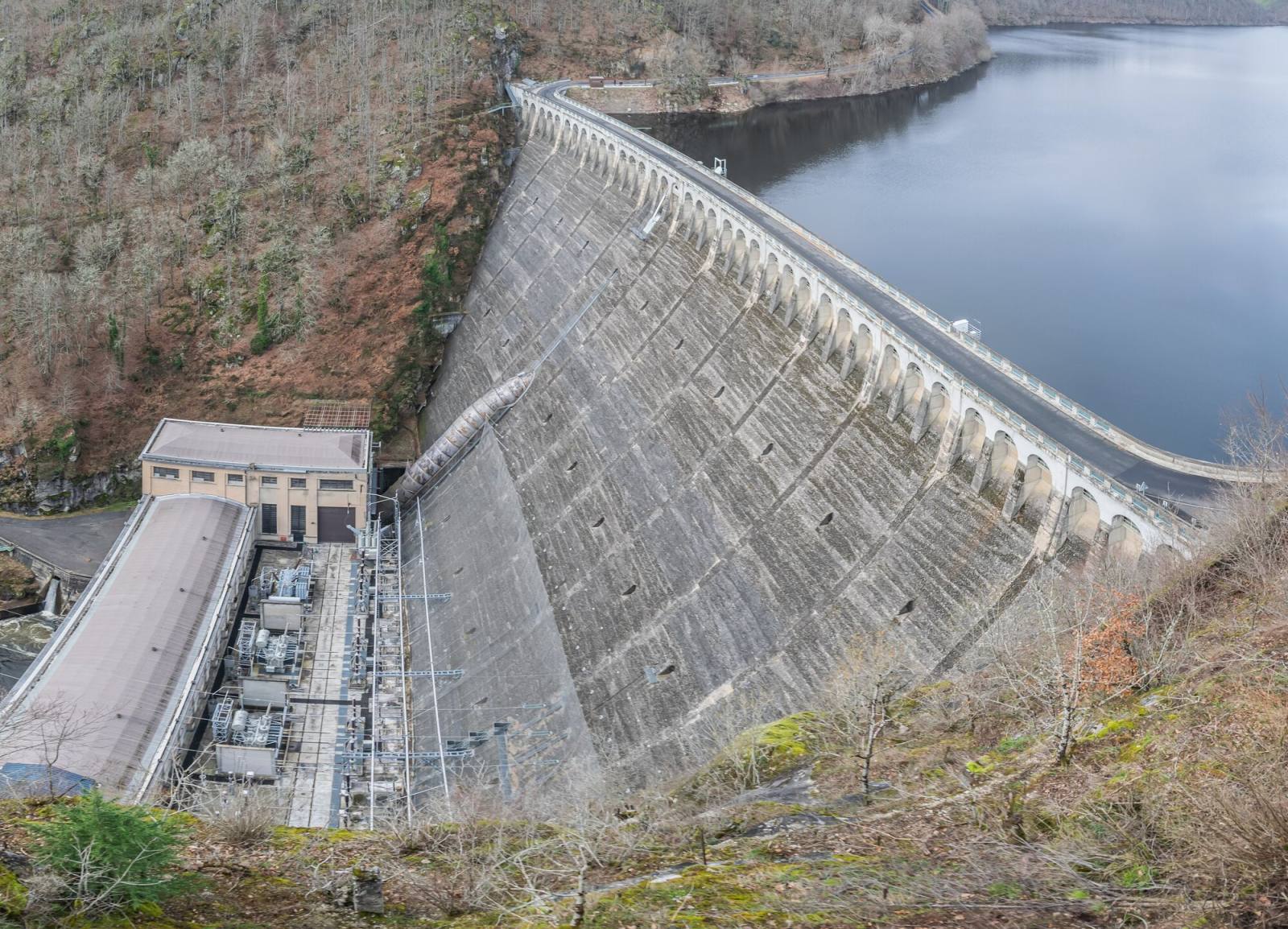 Le mur courbe du barrage de Sarrans et son usine au pied, avec le lac de retenue en amont